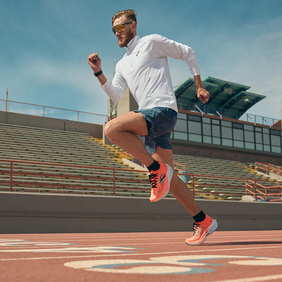 Ein Läufer mit roten Brooks Laufschuhen auf einer Tartanbahn in dynamischem Tempo auf der Zielgeraden. Ansicht von schräg vorn