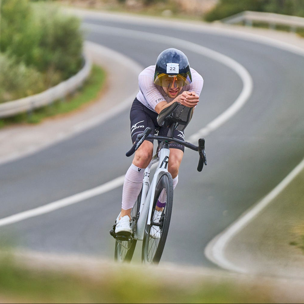 Triathlet Lukas Schnödewind auf seinem Triathlonrad in Aeroposition auf einer kurvigen Straße, Ansicht von schräg vorn
